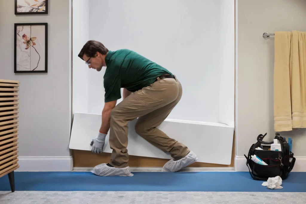 Bath Fitter installer fitting a custom acrylic liner over an existing bathtub, with protective floor covering in place during the installation process