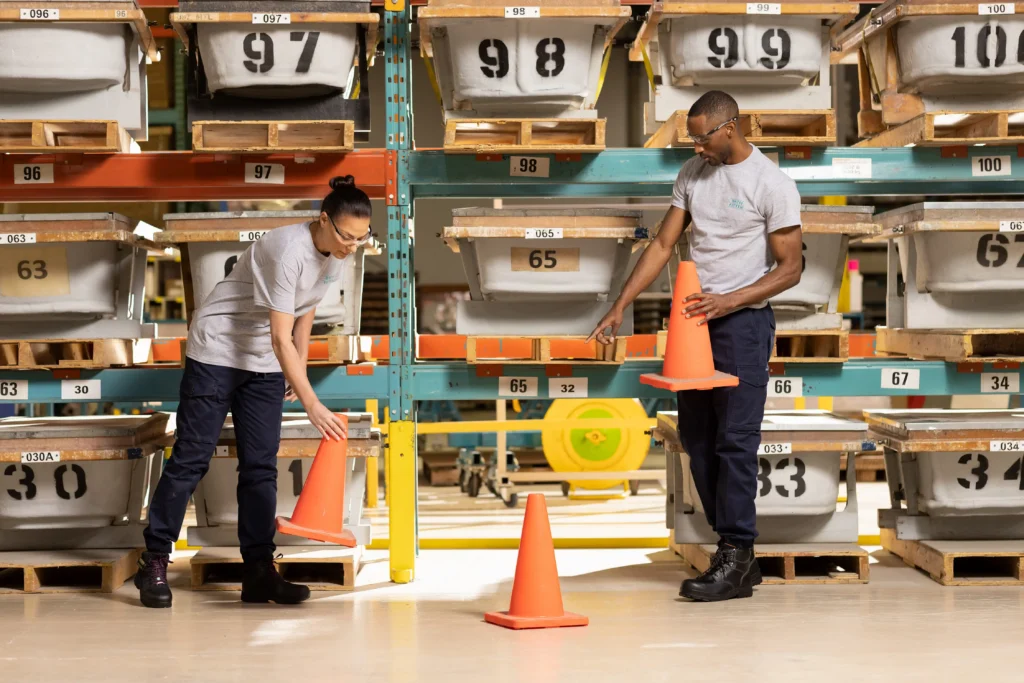 Warehouse workers arranging safety cones in a structured facility storage area, illustrating the manufacturing and quality control process